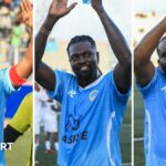 A triptych showing Samuel Eto'o, Emmanuel Adebayor and Jay Jay Okocha wearing light blue football tops and waving to the crowd from the pitch at the Mogadishu National Stadium