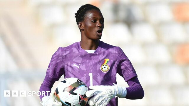 Cynthia Konlan seen from the waist up wearing a purple goalkeeping jersey and white gloves as she carries a football