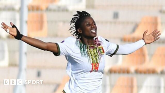 Aissata Traore, wearing a white Mali shirt, spreads her arms out in celebration after scoring against Ghana