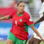 Ibtissam Jraidi in red Morocco shirt and green shorts spreads her arms to her sides and wheels away in celebration as a Mali player in white is seen in the background