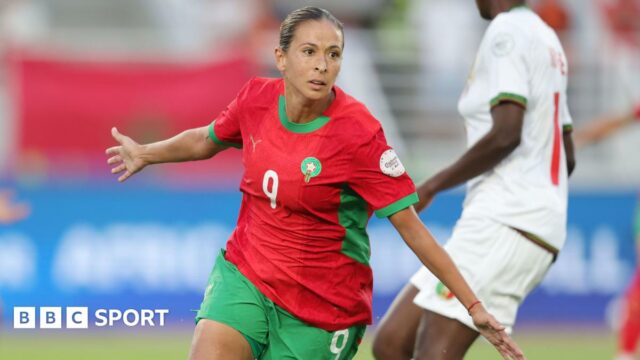 Ibtissam Jraidi in red Morocco shirt and green shorts spreads her arms to her sides and wheels away in celebration as a Mali player in white is seen in the background