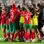 Morocco players and staff celebrate in a huddle on the pitch near the touchline after scoring a late equaliser against Zambia at the 2024 Women's Africa Cup of Nations