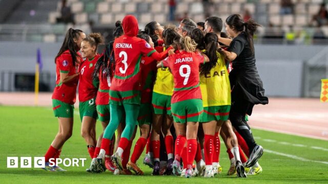 Morocco players and staff celebrate in a huddle on the pitch near the touchline after scoring a late equaliser against Zambia at the 2024 Women's Africa Cup of Nations