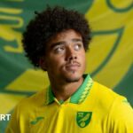 Norwich City striker Jovon Makama, pictured with a club flag.