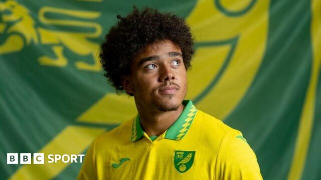 Norwich City striker Jovon Makama, pictured with a club flag.