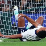 Ollie Watkins lying on the ground and holding his leg in pain after colliding with a goal post during England's match against Wales