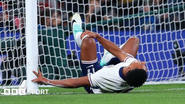 Ollie Watkins lying on the ground and holding his leg in pain after colliding with a goal post during England's match against Wales