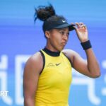 Naomi Osaka looking glum with her hand on her hat