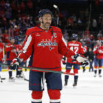 Alex Ovečkin oslovuje Jordana Binningtona, ktorý sa tajne pokúša chytiť do vrecka špeciálny 900. gólový puk NHL