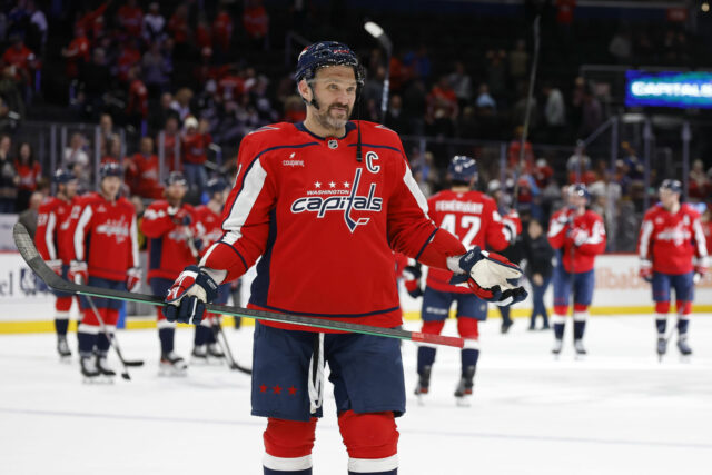 Alex Ovečkin oslovuje Jordana Binningtona, ktorý sa tajne pokúša chytiť Alex Ovečkin oslovuje Jordana Binningtona, ktorý sa tajne pokúša chytiť do vrecka špeciálny 900. gólový puk NHL