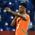 Útočník Pobrežia Slonoviny Amad Diallo v celooranžovom prúžku oslavuje, keď brankár Mozambiku Ernan a Reinildo ležia na zemi.