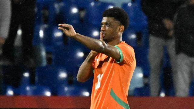 Útočník Pobrežia Slonoviny Amad Diallo v celooranžovom prúžku oslavuje, keď brankár Mozambiku Ernan a Reinildo ležia na zemi.