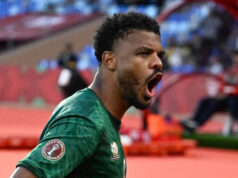 Foster skóroval, keď Juhoafrická republika porazila Zimbabwe a postúpila Usmiaty Oswin Appollis, ktorý je viditeľný od pása nahor, má na sebe zelený dres s krátkym rukávom z Juhoafrickej republiky, zdobený zlatou a s bielym číslom sedem v strede hrude, beží a rozpaží ruky nízko vedľa seba, aby oslávil gól proti Zimbabwe na Afcon 2025. Za ním a naľavo od obrazu je vidieť dvoch spoluhráčov z Južnej Afriky, ktorí ho bežia, aby ho chytili