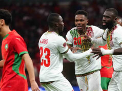 Mali demonštrovali proti Maroku, ktorý hostí Afcon Lassine Sinayoko v bielom drese Mali je vidieť uprostred akcie, keď strieľa penaltu na Africkom pohári národov proti Maroku. Sinayoko práve kopol do lopty, ktorá letí pozdĺž stredu obrazu, len mierne vyvýšená nad sviežim zeleným trávnikom. Päť hráčov je v pozadí na hranici pokutového územia, vrátane dvoch hráčov Mali, z ktorých jeden má ruky zopnuté v modlitbovom geste. Dvaja z troch marockých hráčov v červeno-zelenom už vtrhnú do lóže v očakávaní