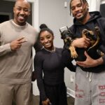 Simone Biles (C) a Jonathan Owens (R) pózujú s chovateľom a ich novým dobermanom, ktorému, ako sa zdá, pri bolestivej procedúre posekali uši.