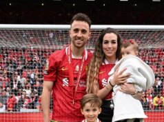 Štvrť Diogo Jota Merseyside je teraz po smrti hviezdy „závojom smútku“. Mužský športovec v červenom drese triumfálne stojí so zdvihnutými rukami a zdanlivo oslavuje významný úspech na ihrisku. Pozadie je plné nadšeného davu, čo naznačuje dôležitosť okamihu.