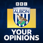 Fotografia Erica Ramsayho v čiernej bunde, ako drží ruky vo vzduchu, zatiaľ čo svetlá štadióna svietia v pozadí