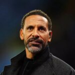 Jednotlivec s bradou a fúzmi, oblečený v čiernej bunde, stojí na poli a pravdepodobne sa venuje športovej aktivite.