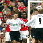 Skupina futbalistov v bielo-červených uniformách oslavuje pred bránkou počas zápasu s veľkým davom divákov v pozadí.