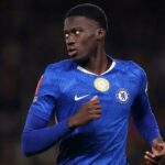 Mamadou Sarr je zobrazený od pása nahor, ako po finále Afcon 2025 objíma senegalského tímového kolegu Abdoulayeho Secka. Sarr je napravo z dvojice s rukami vysoko okolo Seckovej hornej časti chrbta a možno ho vidieť kričať s otvorenými ústami a zatvorenými očami, zatiaľ čo poloha jeho hlavy zakrýva Seckovu tvár. Obaja sú v zelených dresoch Senegalu a okolo nich vidno padať veľké kvapky dažďa