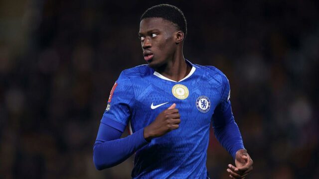 Mamadou Sarr je zobrazený od pása nahor, ako po finále Afcon 2025 objíma senegalského tímového kolegu Abdoulayeho Secka. Sarr je napravo z dvojice s rukami vysoko okolo Seckovej hornej časti chrbta a možno ho vidieť kričať s otvorenými ústami a zatvorenými očami, zatiaľ čo poloha jeho hlavy zakrýva Seckovu tvár. Obaja sú v zelených dresoch Senegalu a okolo nich vidno padať veľké kvapky dažďa