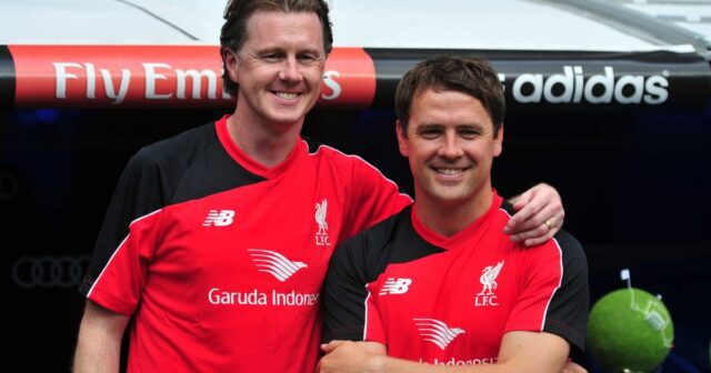 Dve osoby oblečené v červených dresoch stoja blízko pri sebe a vyzerajú ako v oslavnej póze s transparentom v pozadí s nápisom 