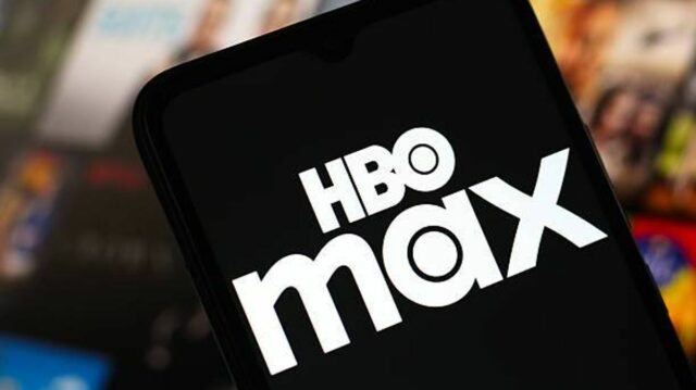 Detailný pohľad na smartfón s logom HBO Max na obrazovke. Pozadie je rozmazané a zobrazuje rôzne zábavné médiá v okolí.