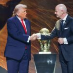 Jednotlivec v spoločenskom oblečení, stojaci na tmavom pozadí a v ruke drží zlatú trofej.