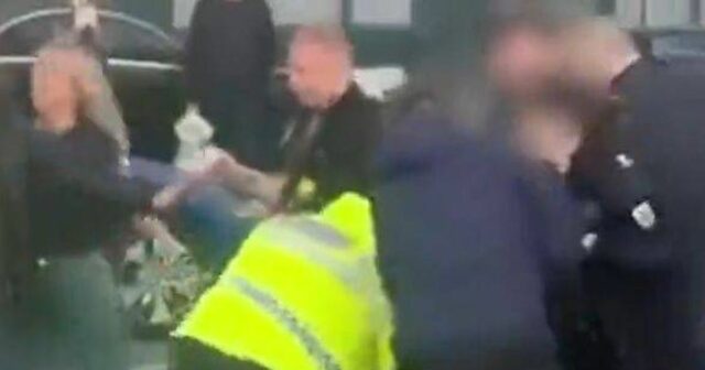 V preplnenej scéne je jednotlivec oblečený vo vysoko viditeľnej žltej veste zapojený do konfrontácie s inou osobou, zatiaľ čo tretí jednotlivec, oblečený v čiernom, zrejme zasahuje. Prostredie naznačuje napäté a možno rušivé prostredie.