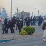 Skupinu jednotlivcov, oblečených v červeno-bielych dresoch, vidno kráčať po ulici. Zdá sa, že sú zapojení do sprievodu s rôznymi štruktúrami a semaforom viditeľným v pozadí. Obloha hore je polooblačná.