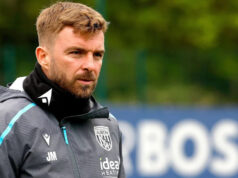 Ste spokojný s Morrisonovým vymenovaním? James Morrison v sivej teplákovej súprave West Bromwich Albion a čiernych nohaviciach na tréningu so slovom "BOSS" vidieť na rozmazanej reklamnej tabuli v diaľke za ním.