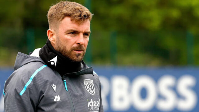 James Morrison v sivej teplákovej súprave West Bromwich Albion a čiernych nohaviciach na tréningu so slovom "BOSS" vidieť na rozmazanej reklamnej tabuli v diaľke za ním.