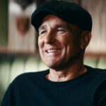 Vinnie Jones sa usmieva v čiernej mikine a plochej šiltovke