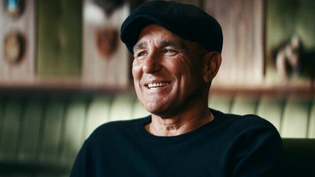 Vinnie Jones sa usmieva v čiernej mikine a plochej šiltovke