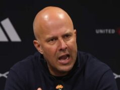 Arne Slot po porážke v Man Utd zúrivo kritizuje „VAR proti nám celú sezónu“. Jednotlivec, oblečený v námorníckej modrej košeli, je zapojený do tlačovej konferencie. Na pozadí je výrazné logo a textová značka.
