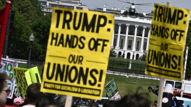 Demonštranti držia znamenia počas prvomájového zhromaždenia, ktoré si pripomína Medzinárodný deň pracujúcich ako Marine One, s americkým prezidentom Donaldom Trumpom na palube, ktorý odchádza z južného trávnika Bieleho domu vo Washingtone, DC, 1. mája 2026. Trump ide na Floridu, aby vystúpil na podujatí v The Villages a zúčastnil sa večere Forum Club of the Palm Beaches
