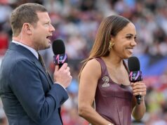 Čas výkopu SoccerAid 2026 sa posunul, pretože ITV potvrdila kompletné zostavy tímov pred zápasom Jednotlivec v formálnom oblečení, pravdepodobne športový komentátor, stojí vedľa ženy oblečenej v tope bez rukávov, obaja držia mikrofóny a oslovujú publikum na štadióne.