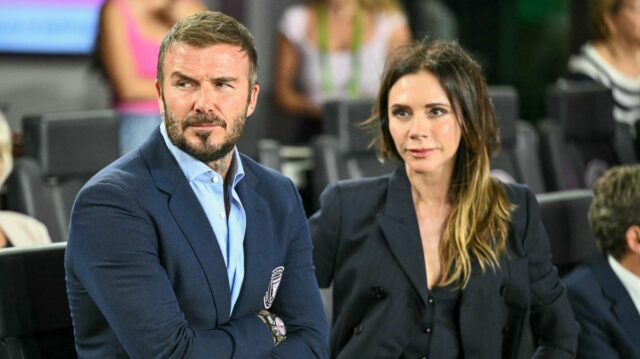David a Victoria Beckhamovci ako pár na druhom mieste v Obraz zobrazuje muža a ženu stojacich blízko, pravdepodobne na spoločenskej udalosti. Muž má na sebe okuliare a modrý kabát, žena má športové slnečné okuliare a biely top. V pozadí sú viditeľné rozmazané postavy, čo naznačuje preplnené prostredie.