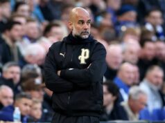 Pep Guardiola je „extrémne sklamaný“, keď Gary Neville „prekvapil“ únikom informácií z Man City Muž, pravdepodobne tréner alebo manažér, stojí na okraji športového ihriska so skríženými rukami a pozorne sleduje prebiehajúcu hru. Scéna sa odohráva na štadióne plnom veľkého davu divákov, ktorí sa všetci sústredia na zápas.