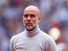 Pep Guardiola sa rozhodol prelomiť mlčanie o „ukončení“ nárokov niekoľko dní po „útočení“ Jednotlivec s holou hlavou, odetý v bielom roláku, stojí v popredí, s rozmazaným publikom viditeľným v pozadí, čo naznačuje formálne alebo profesionálne prostredie.