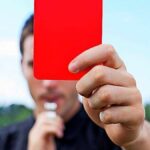 Jednotlivec, ktorý drží v rukách červenú kartu, čo pravdepodobne znamená disciplinárne opatrenie alebo varovanie.