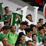 Mexickí fanúšikovia držiaci listy s nápisom Mexiko povzbudzujúc na futbalovom štadióne.