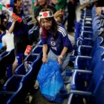 Žena nosí futbalový dres a čelenku a nesie vrece na odpadky v uličke na štadióne
