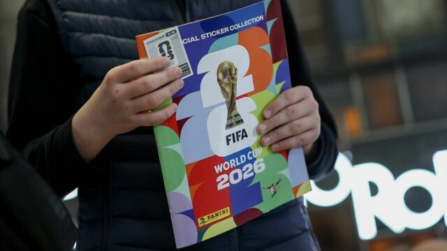 Ponuka nálepiek na Majstrovstvá sveta Panini dáva fanúšikom 112 nálepiek Osoba oblečená v tmavom saku drží farebnú brožúru s logom Majstrovstiev sveta vo futbale 2026.