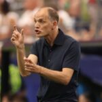 Futbalista v žltom drese kľačí na ihrisku, pravdepodobne v súťažnom zápase, s divákmi v pozadí.