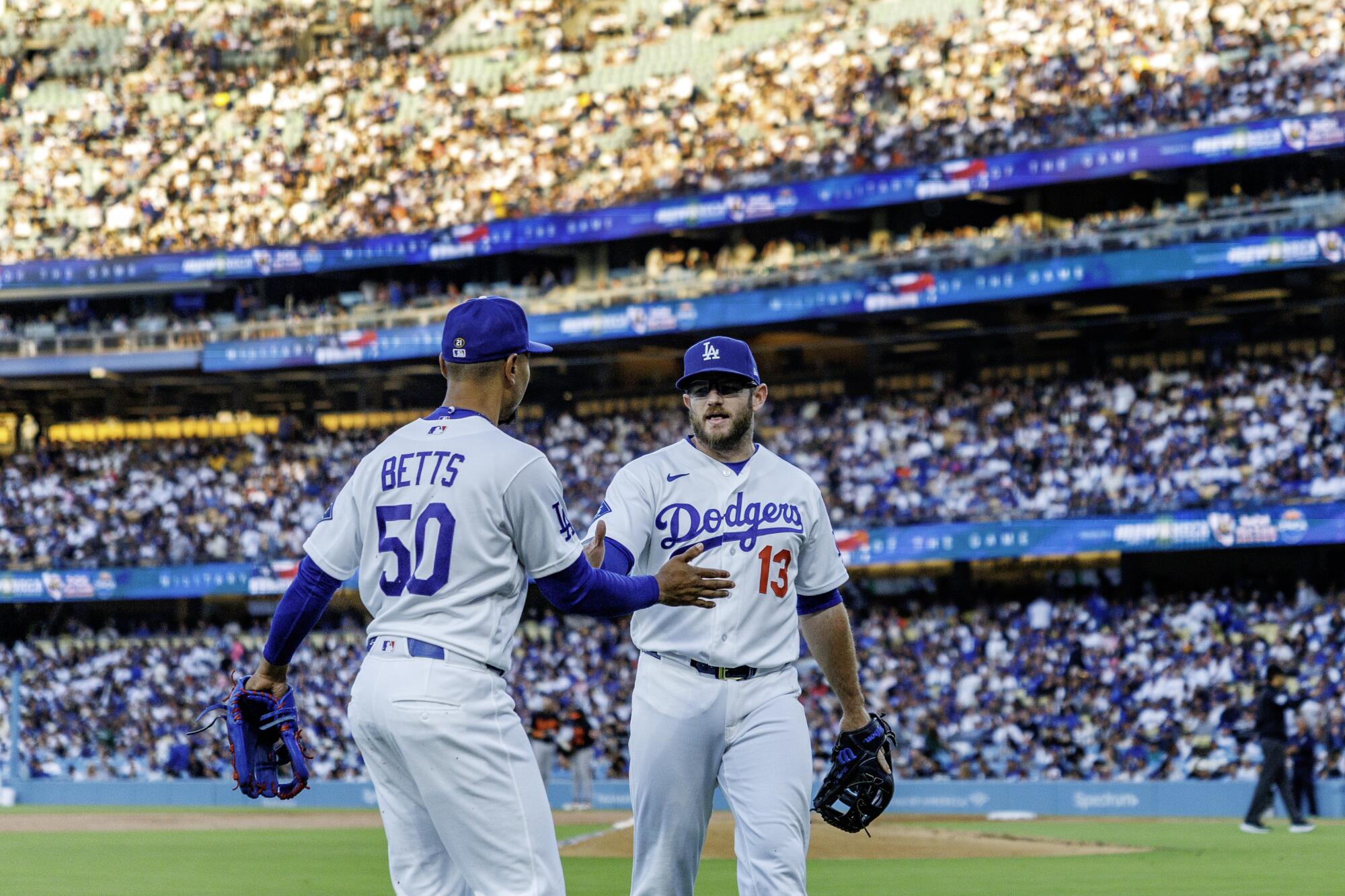 Kraťas Dodgers Mookie Betts, vľavo, a tretí hráč na ihrisku Max Muncy si blahoželajú po defenzívnej hre minulý mesiac.