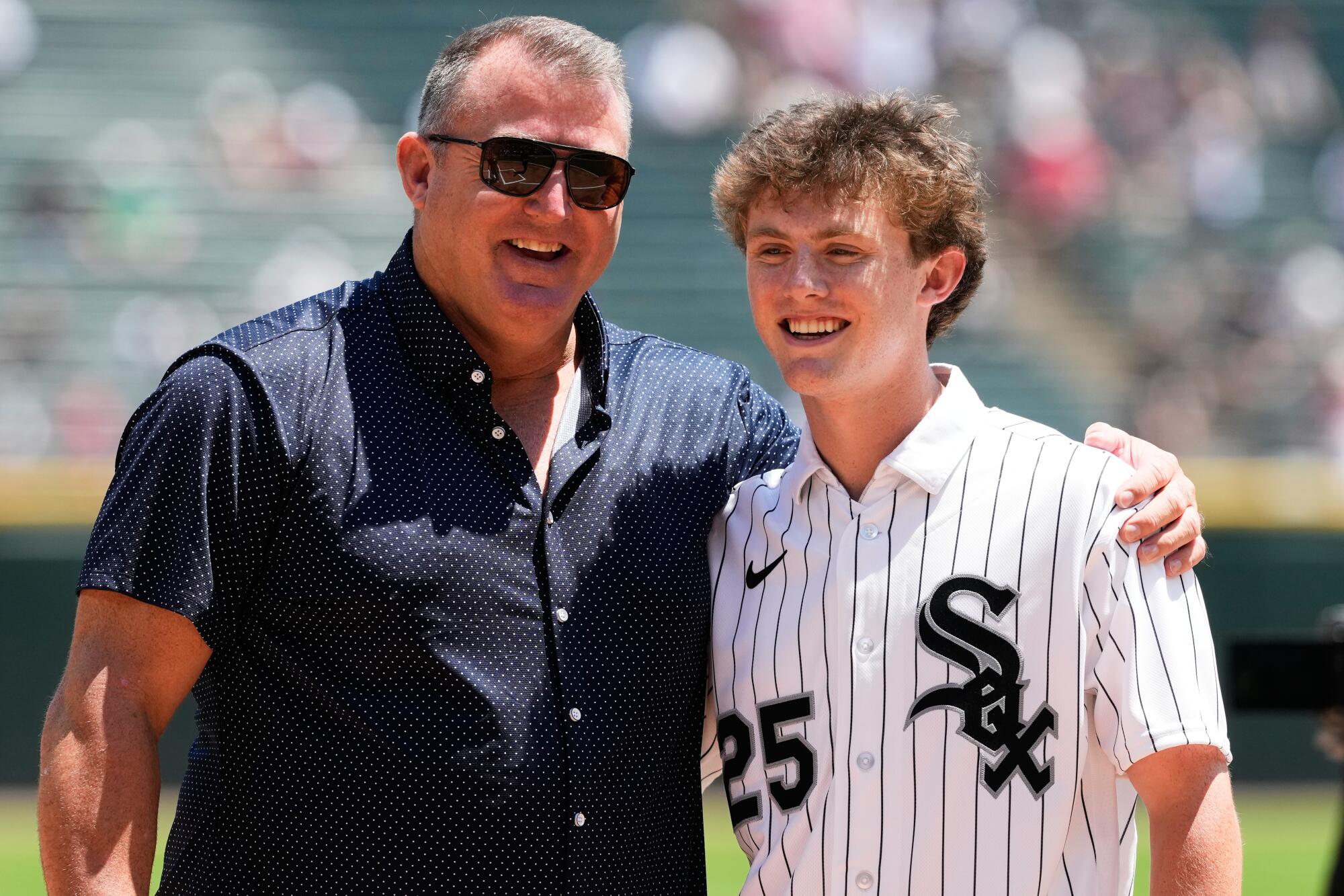 Jim Thome v tmavej košeli s krátkymi rukávmi má jednu ruku okolo svojho syna Landona, oblečeného v póle White Sox