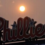 Slnko svieti na oranžovo pri výsledkovej tabuli Phillies počas bejzbalového zápasu vo Philadelphii.