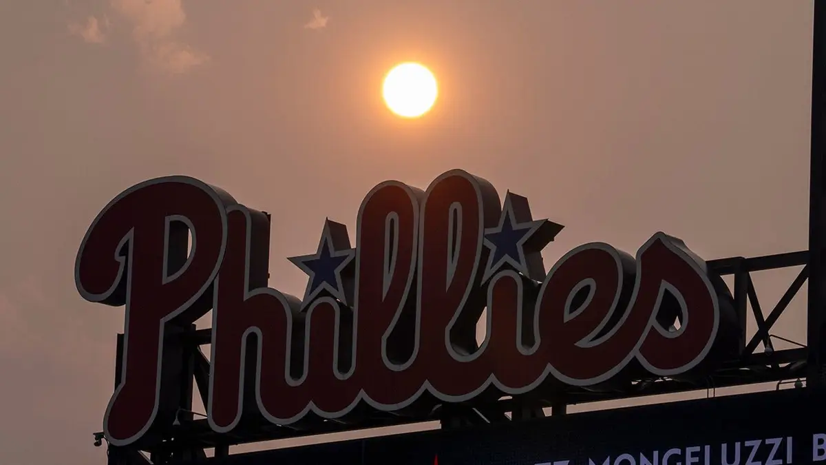 Slnko svieti na oranžovo pri výsledkovej tabuli Phillies počas bejzbalového zápasu vo Philadelphii.