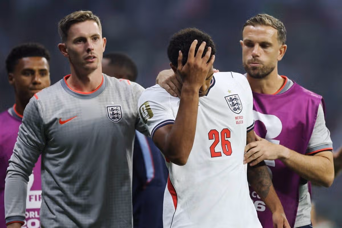 Futbalisti v tímových dresoch stoja na ihrisku. Jeden hráč sa drží rukou za hlavu, pravdepodobne v dôsledku faulu alebo zranenia,